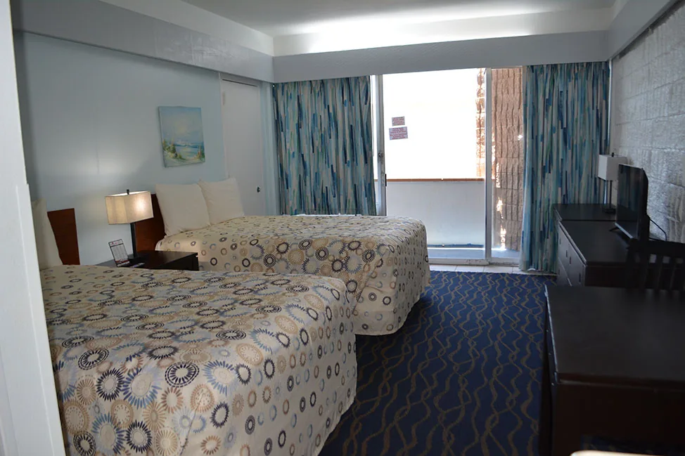 A room with two beds, a dresser with a TV and curtains open to the balcony