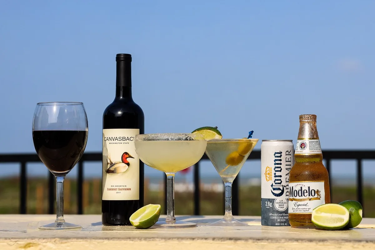 A glass of red wine, a bottle, a margarita, a martini, a Corona Premier and a Modelo on the deck rail