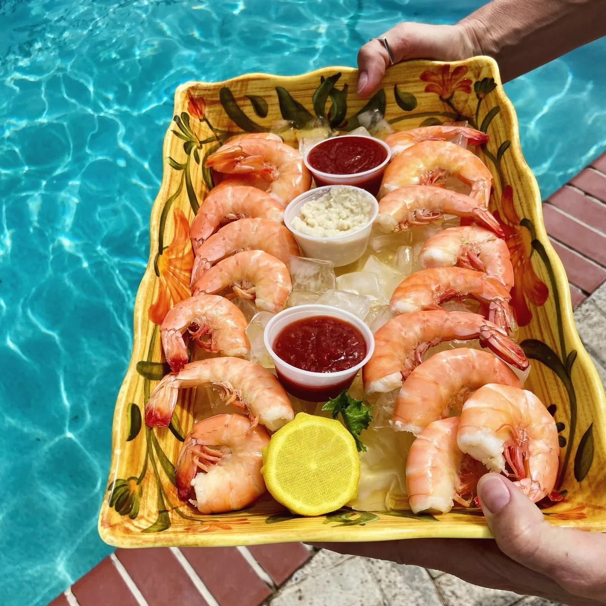 A tray of chilled Gulf shrimp on ice with cocktail sauce, horseradish and lemon, held over the pool