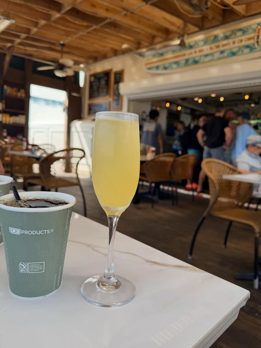 A mimosa in a flute and a cup of coffee on a table in the cafe, with the bar behind