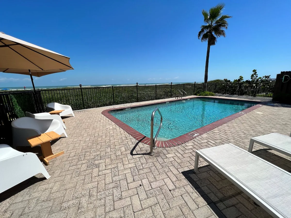 The pool deck with lounge chairs and an umbrella by the dunes