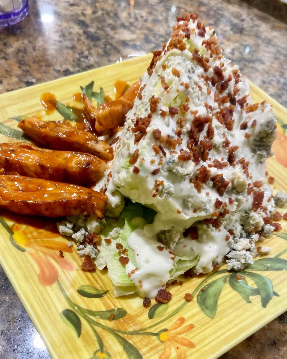 An iceberg wedge salad with blue cheese dressing, blue cheese crumbles and bacon, served with buffalo chicken
