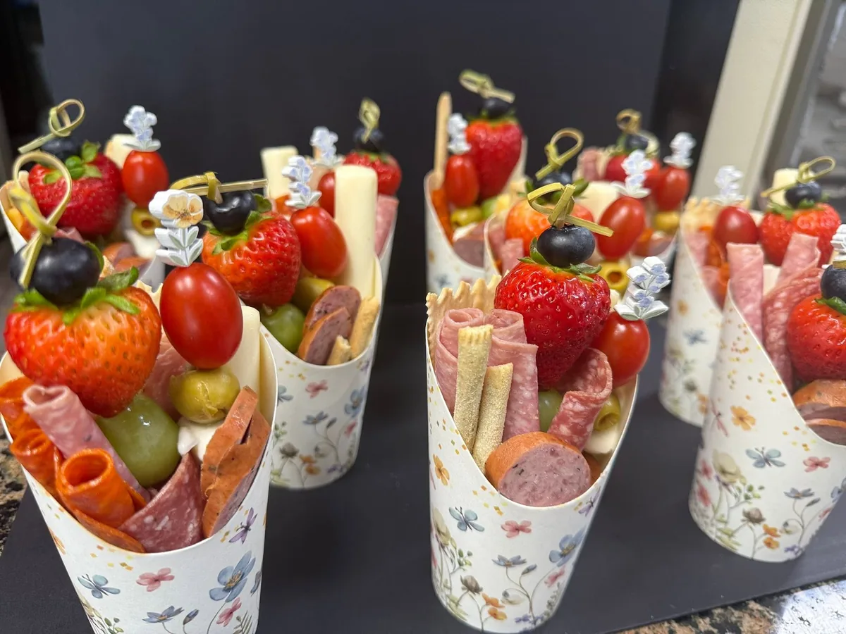 Charcuterie cups with salami, cheese sticks, strawberries, tomatoes and olives on skewers