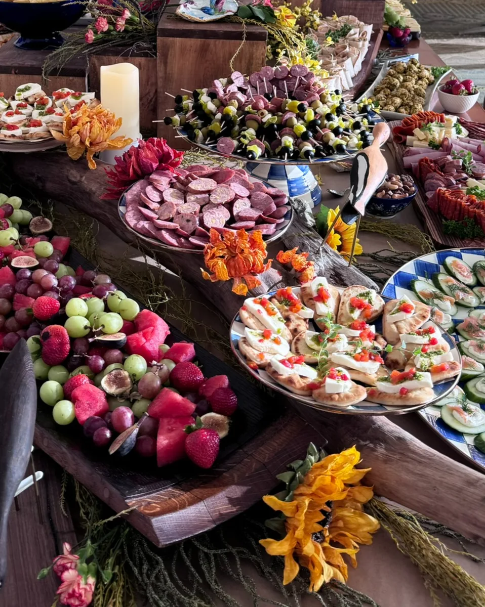 A long grazing table of fruit, meats, cheeses and hors d’oeuvres decorated with orange flowers