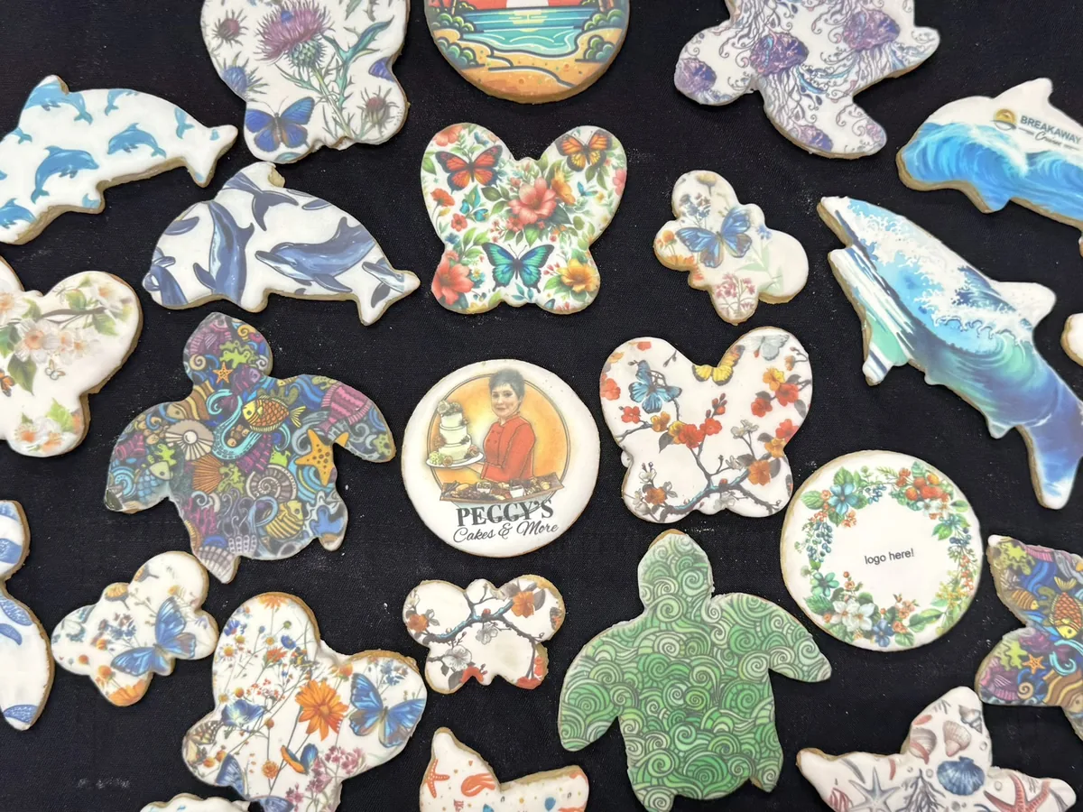 Printed cookies cut as dolphins, sea turtles and butterflies, with one printed with the Peggy's Cakes & More logo