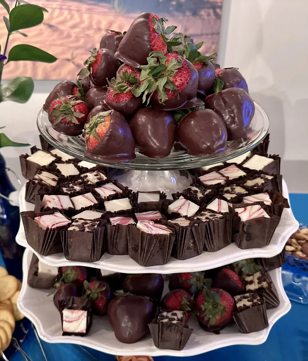 A tiered stand of chocolate-covered strawberries over rows of brownie bites