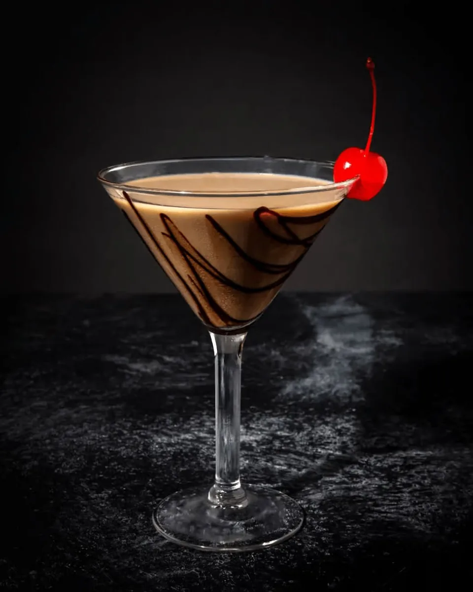 A chocolate martini with chocolate swirls on the glass and a cherry