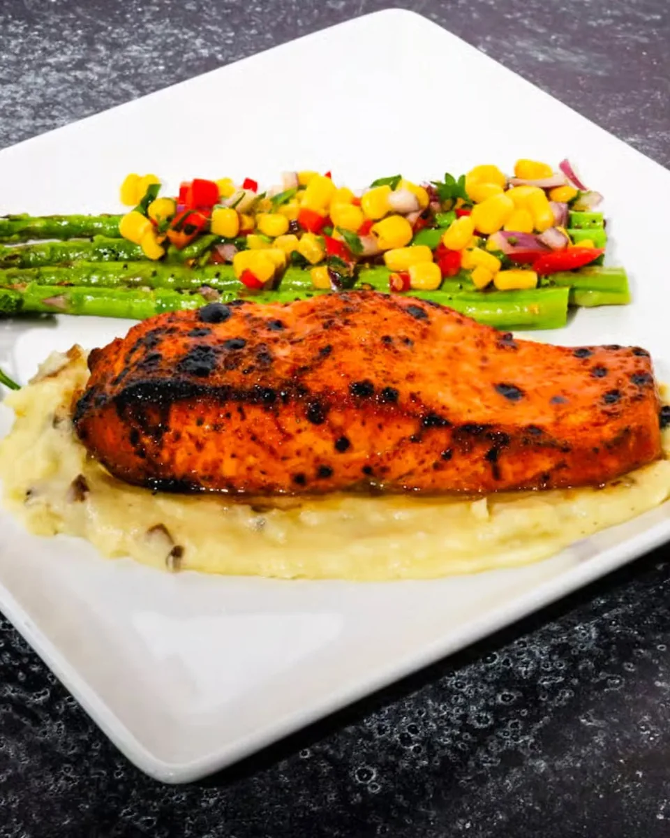 A seared salmon fillet on mashed potatoes with grilled asparagus and a corn and pepper relish