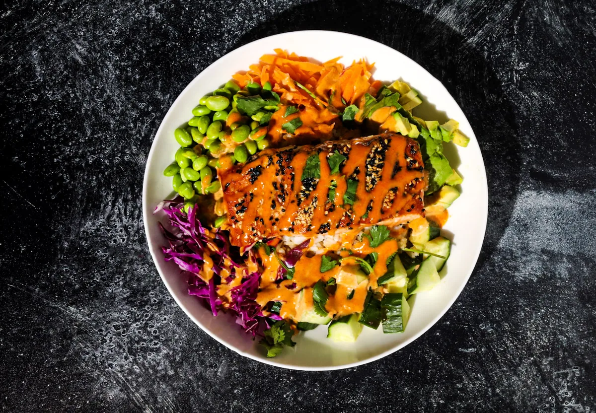Seared salmon over greens with edamame, red cabbage, carrots and cucumber, with a spicy drizzle