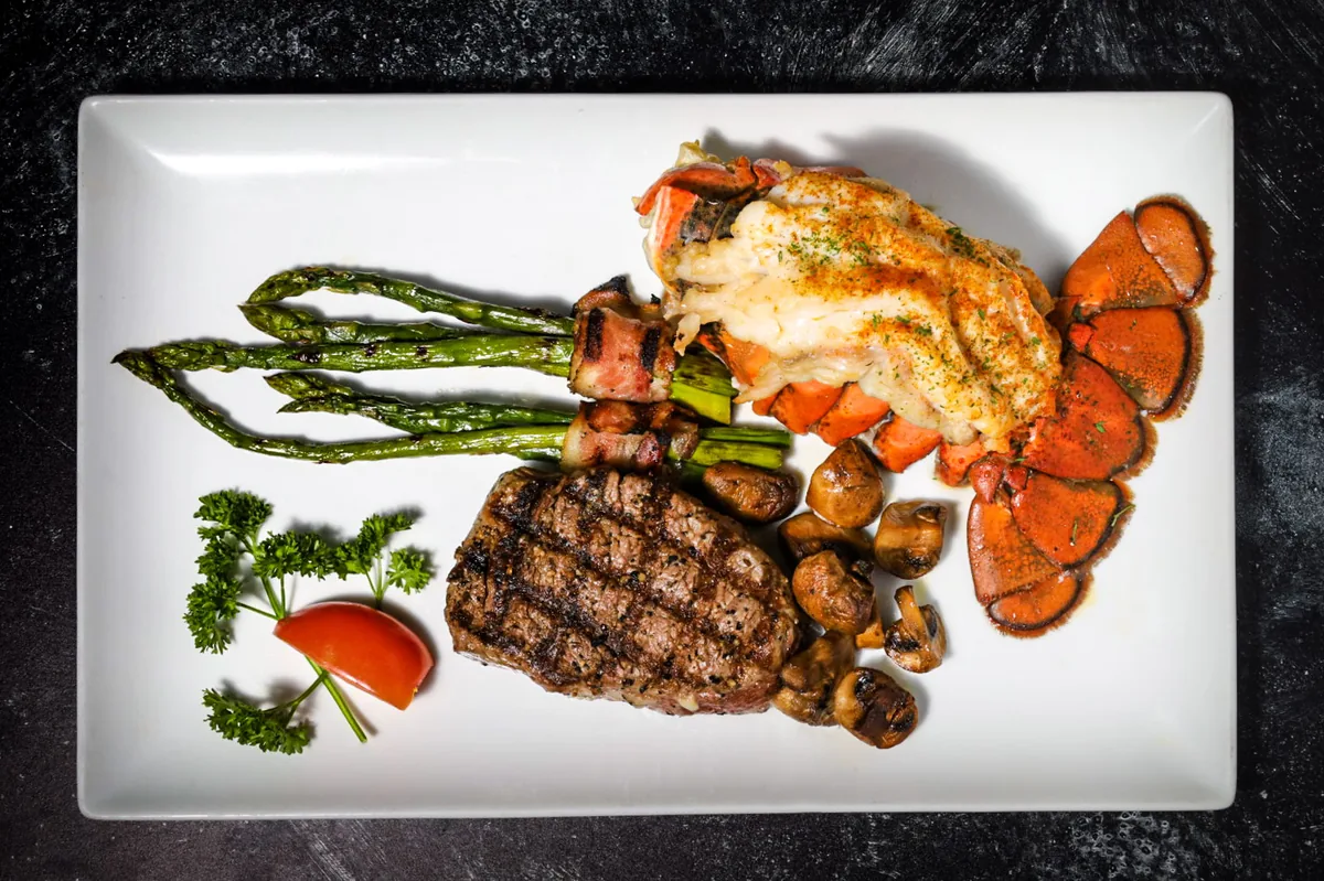 A grilled steak with a broiled lobster tail, bacon-wrapped asparagus and mushrooms