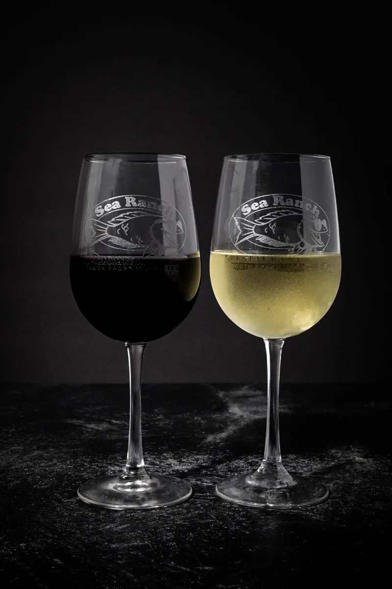 A glass of red wine and a glass of white wine, both etched with the Sea Ranch logo