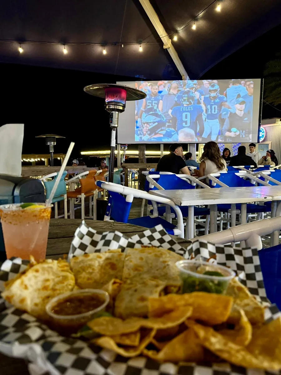 A quesadilla with chips, salsa and guacamole on the deck at night, with a game on the big screen