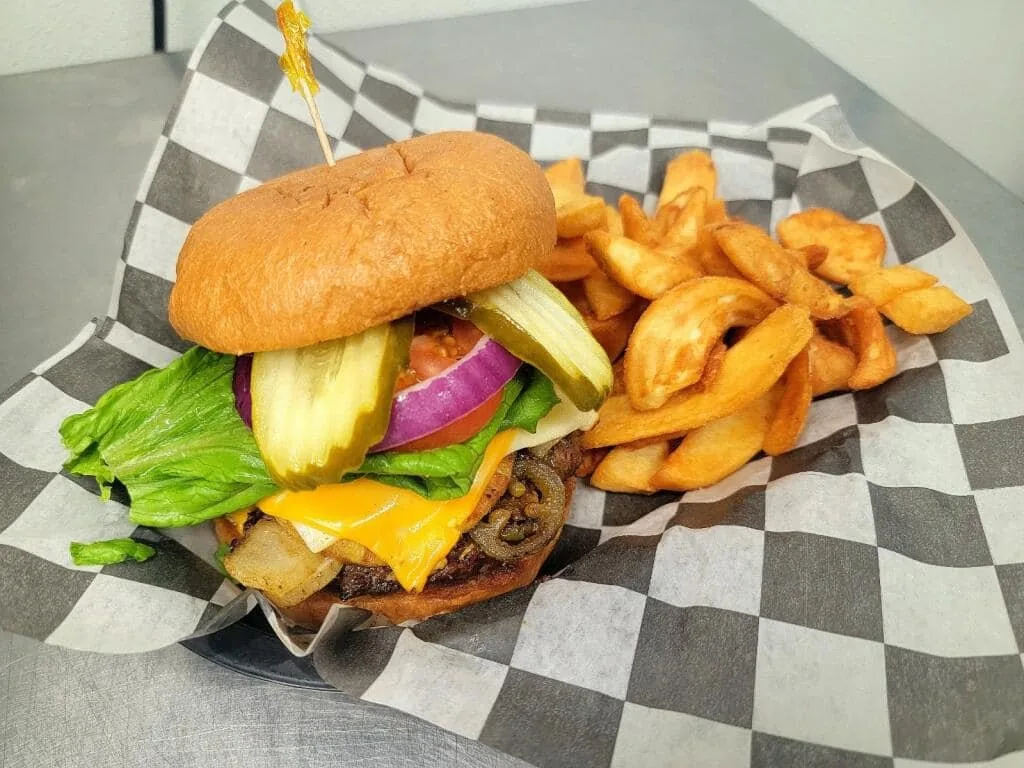 A burger with cheese, grilled jalapenos and onions, lettuce, tomato and pickles, with wedge fries