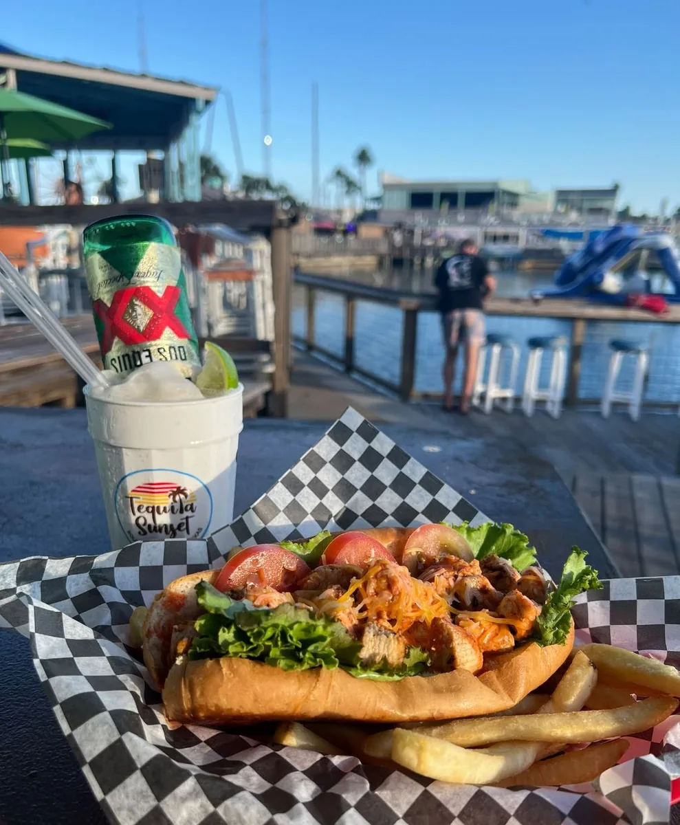 A sandwich with fries and a frozen margarita topped with a Dos Equis, by the marina