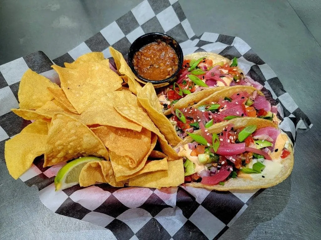 Three tacos with pickled red onion, pico de gallo, green onion, sesame seeds and a creamy sauce, with chips and salsa
