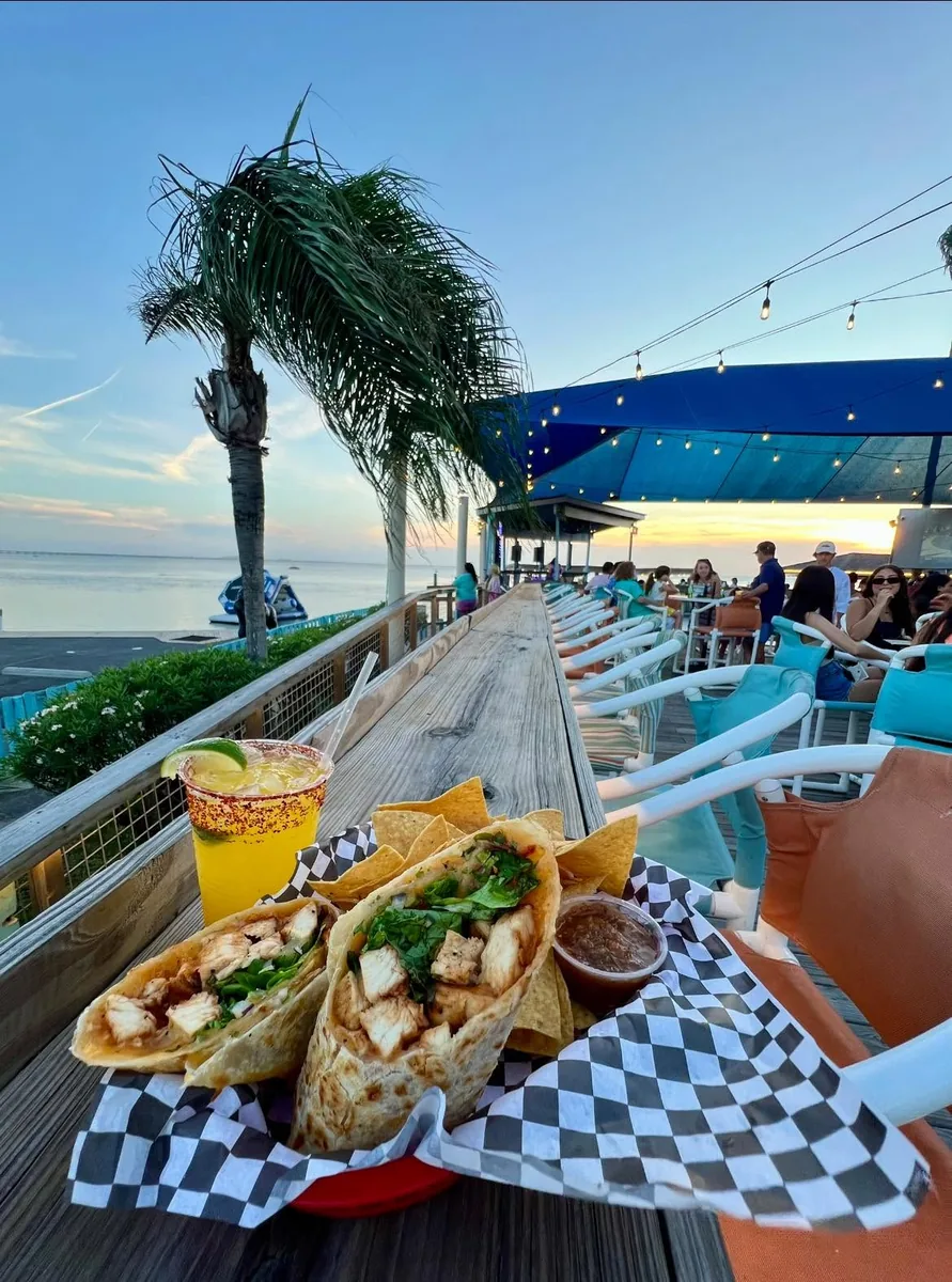A chicken wrap with chips and salsa and a chili-rimmed drink on the rail over the bay at sunset