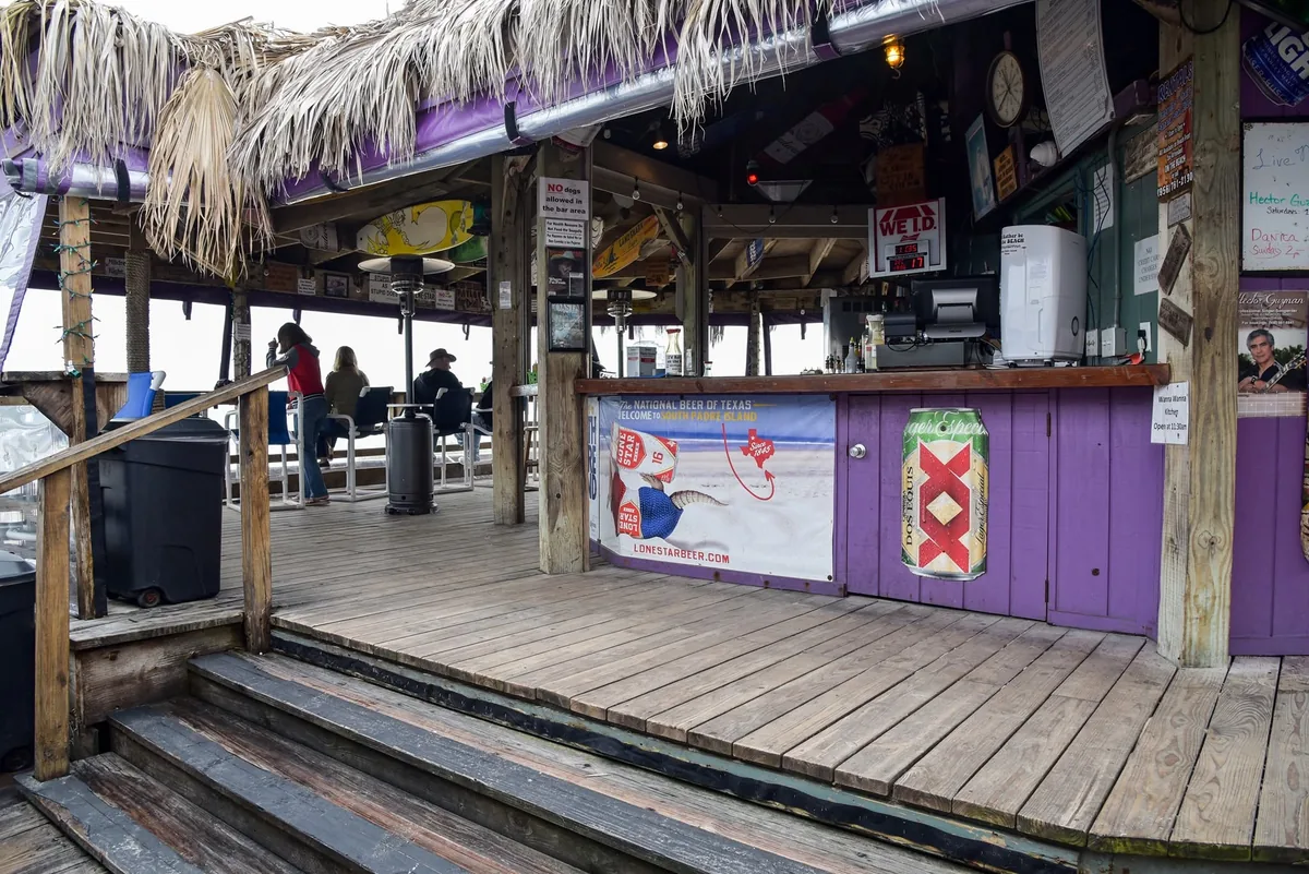 The purple bar counter under a palm-thatch roof, with steps up from the wooden deck