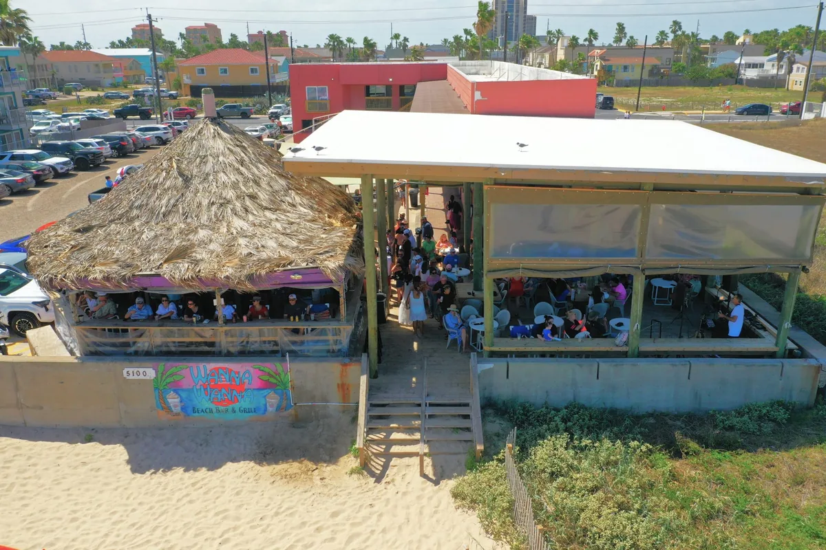 An aerial view of the beach bar with its thatched roof and covered deck above the sand