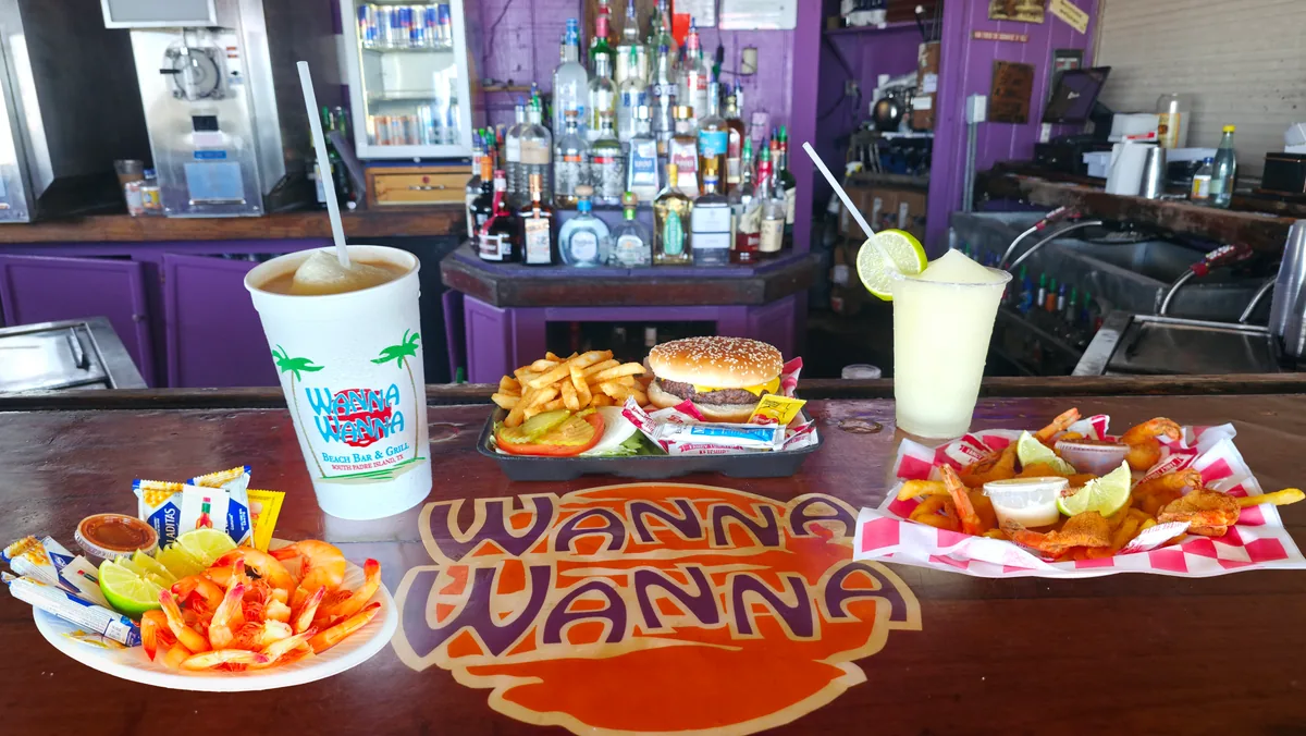 A spread on the bar: peel-and-eat shrimp, a burger with fries, a fried shrimp basket, a margarita and a frozen drink in a Wanna Wanna cup