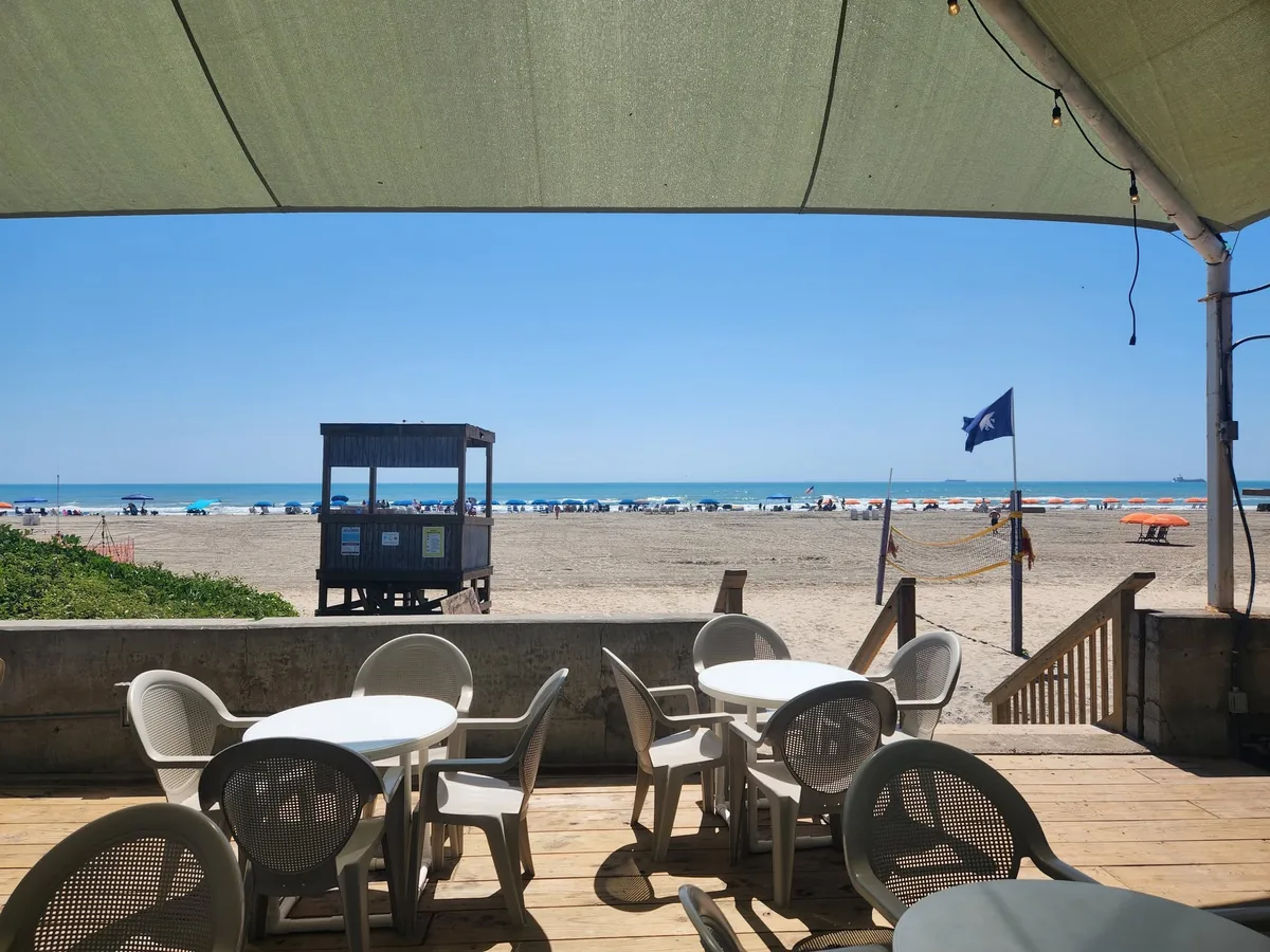 Tables and chairs on the shaded deck looking out over the beach and a lifeguard stand