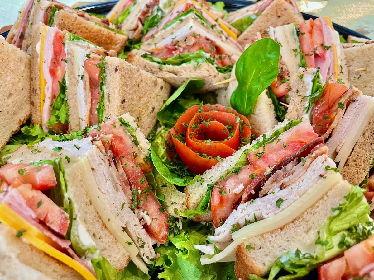 A platter of club sandwich quarters with turkey, ham, bacon, cheese, tomato and lettuce around a tomato rose