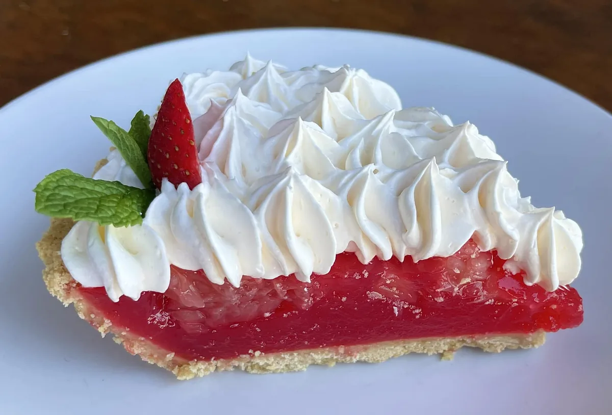A slice of ruby-red grapefruit pie topped with piped whipped cream, a strawberry and mint