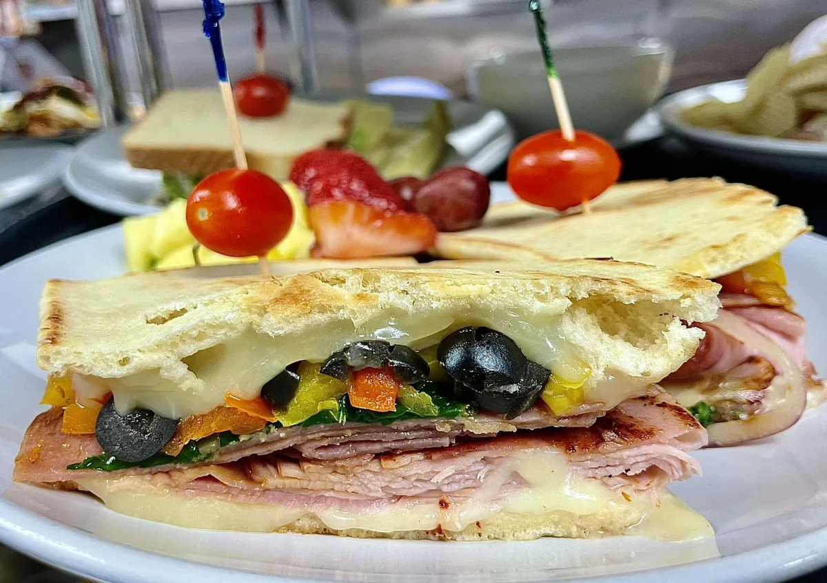 A pressed panini with ham, melted cheese, black olives, peppers and spinach, with fruit on the side