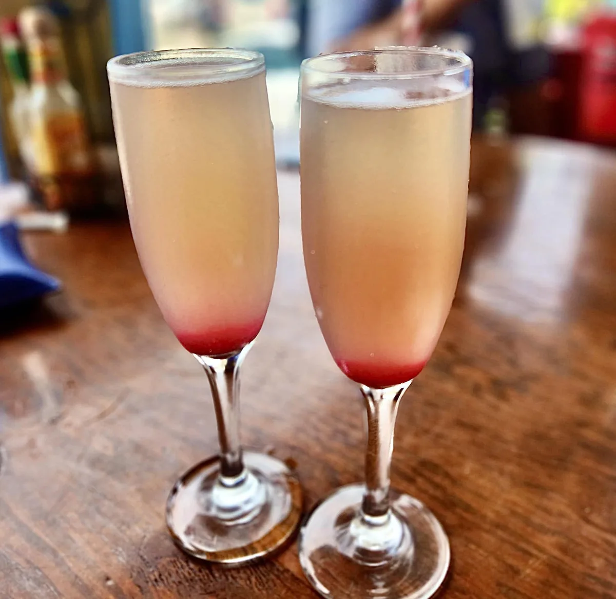 Two mimosas in champagne flutes with a red layer at the bottom, on a wooden table