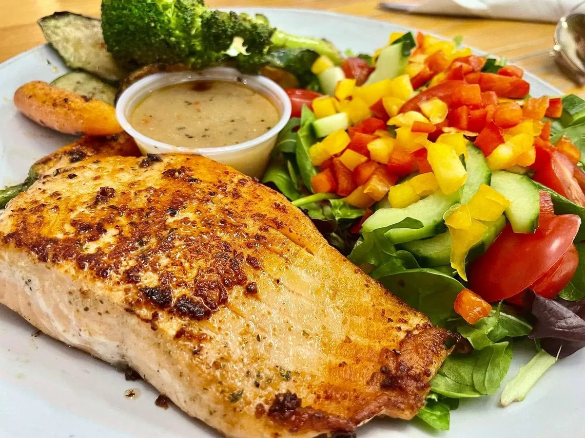 A seared salmon fillet with a salad of peppers, cucumber and tomato, roasted vegetables and a cup of dressing