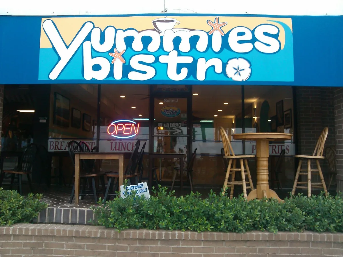 The Yummies Bistro storefront with its blue and yellow awning sign, an OPEN sign and patio tables out front